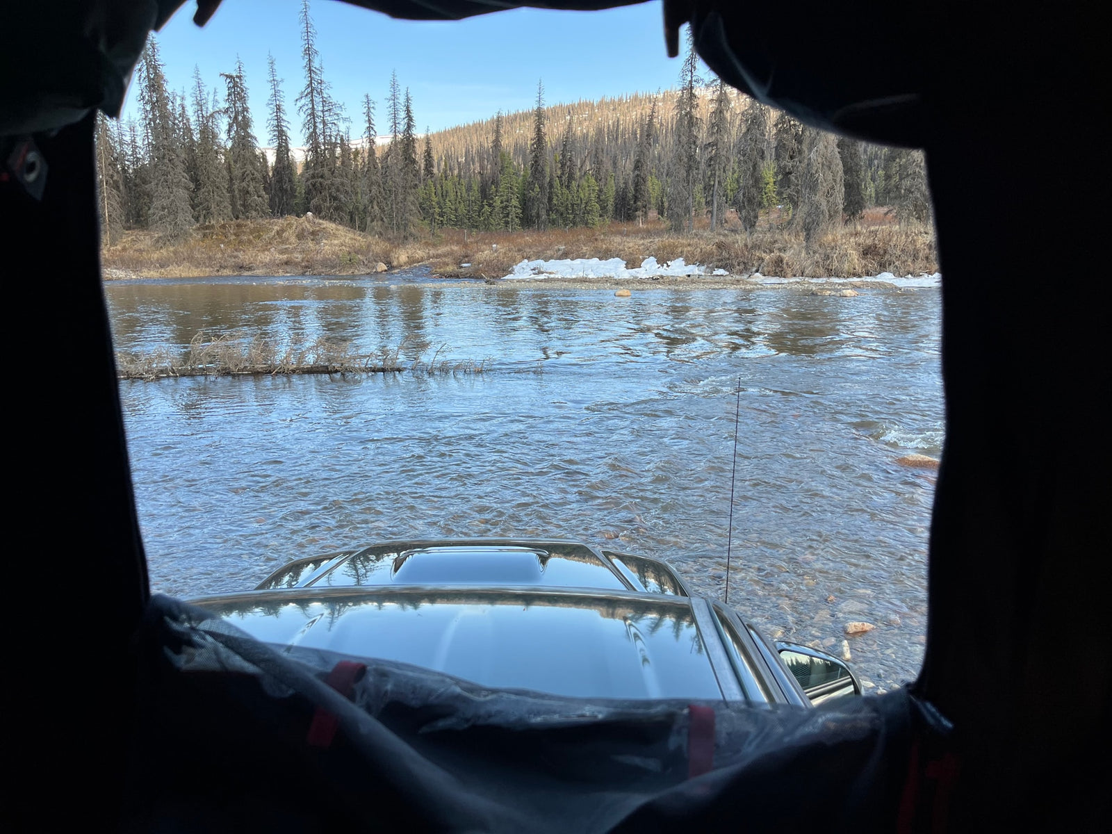 View from an RV rental's window: a vehicle crossing a shallow river, surrounded by a winter forest.