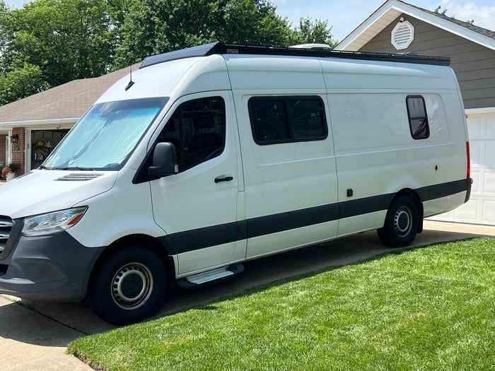 A white Mercedes Sprinter camper van for RV rental, parked on a sunny driveway, ready for adventure travel.