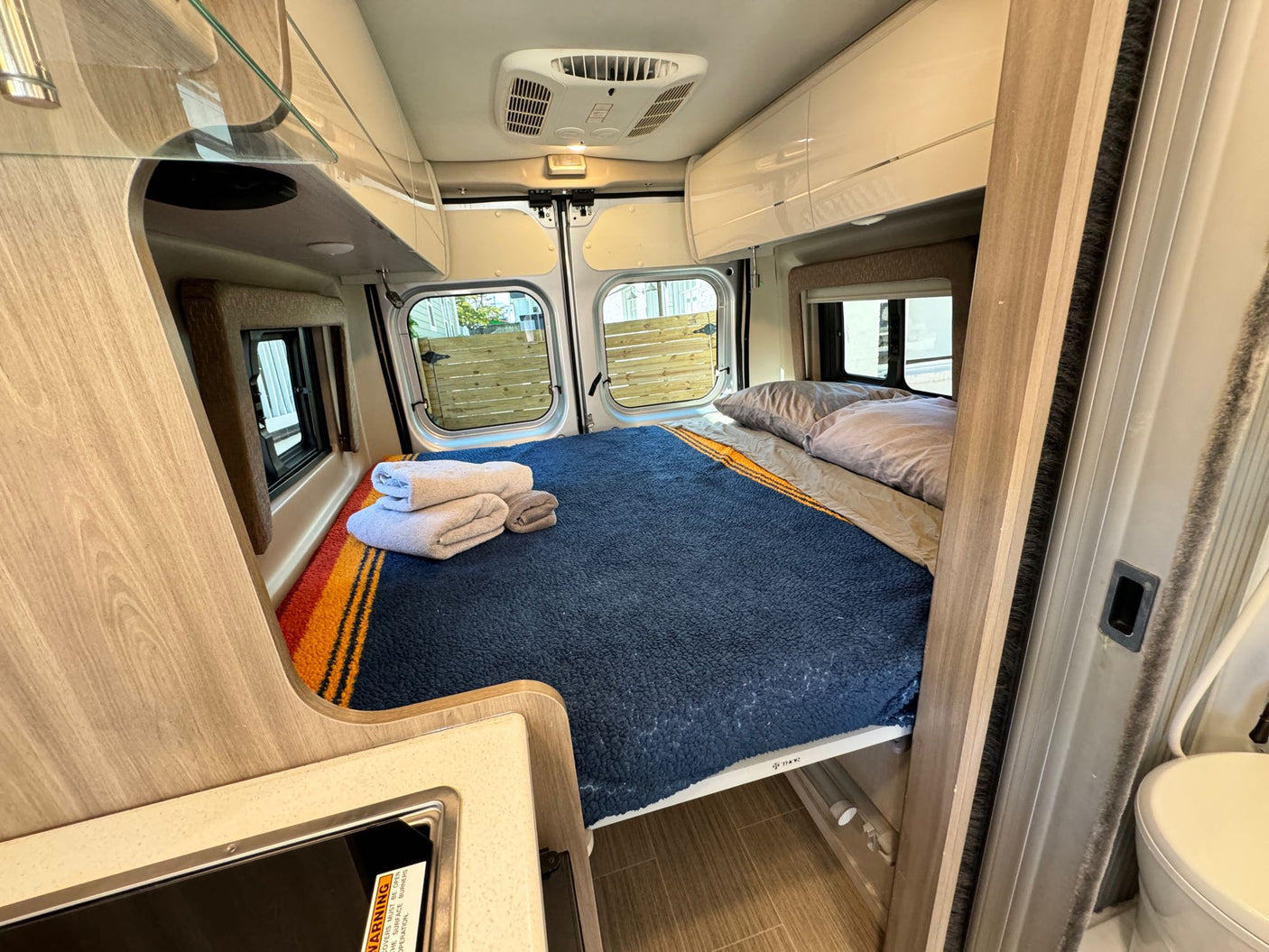 and overhead storage.|Cozy RV rental interior with a bed featuring a blue blanket
