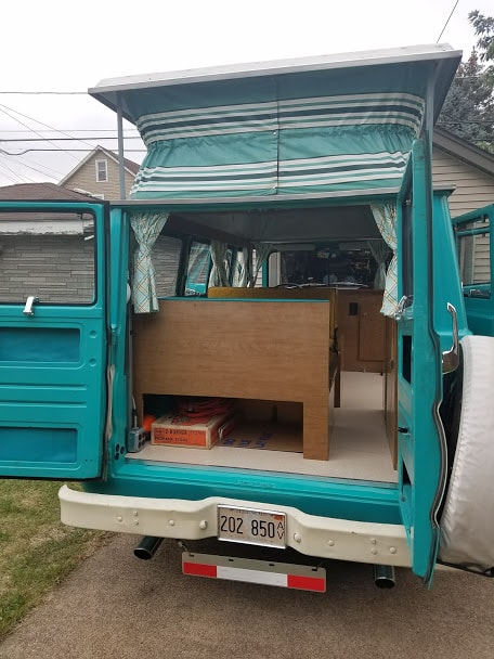 spare tire. Great RV rental option!|Rear view of a vintage teal pop-top camper van with open doors