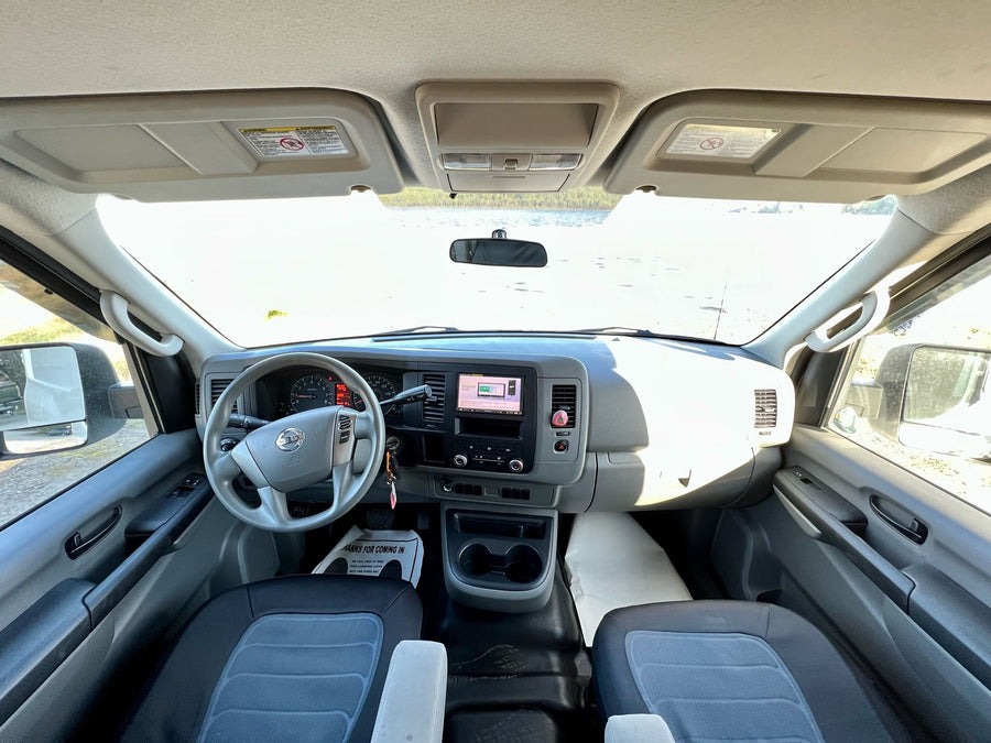 and a tranquil lake seen through the windshield.|Inside a Nissan NV dashboard