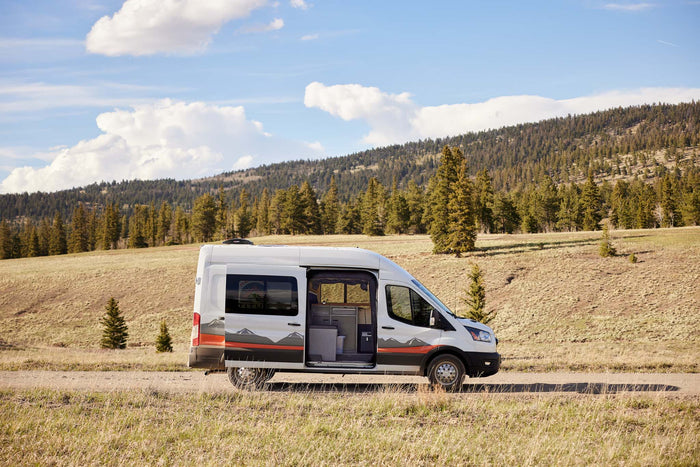 White camper van on a dirt road amidst mountains, perfect for your next rv rental adventure.