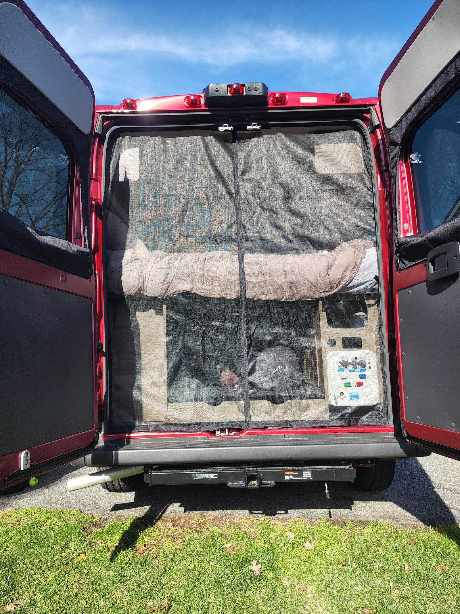 Inside an RV rental van: rear view showing mesh screen, sleeping area, and control panel.