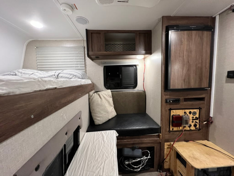 Cozy RV rental interior with bunk bed, dinette, compact fridge, and a custom power management display.