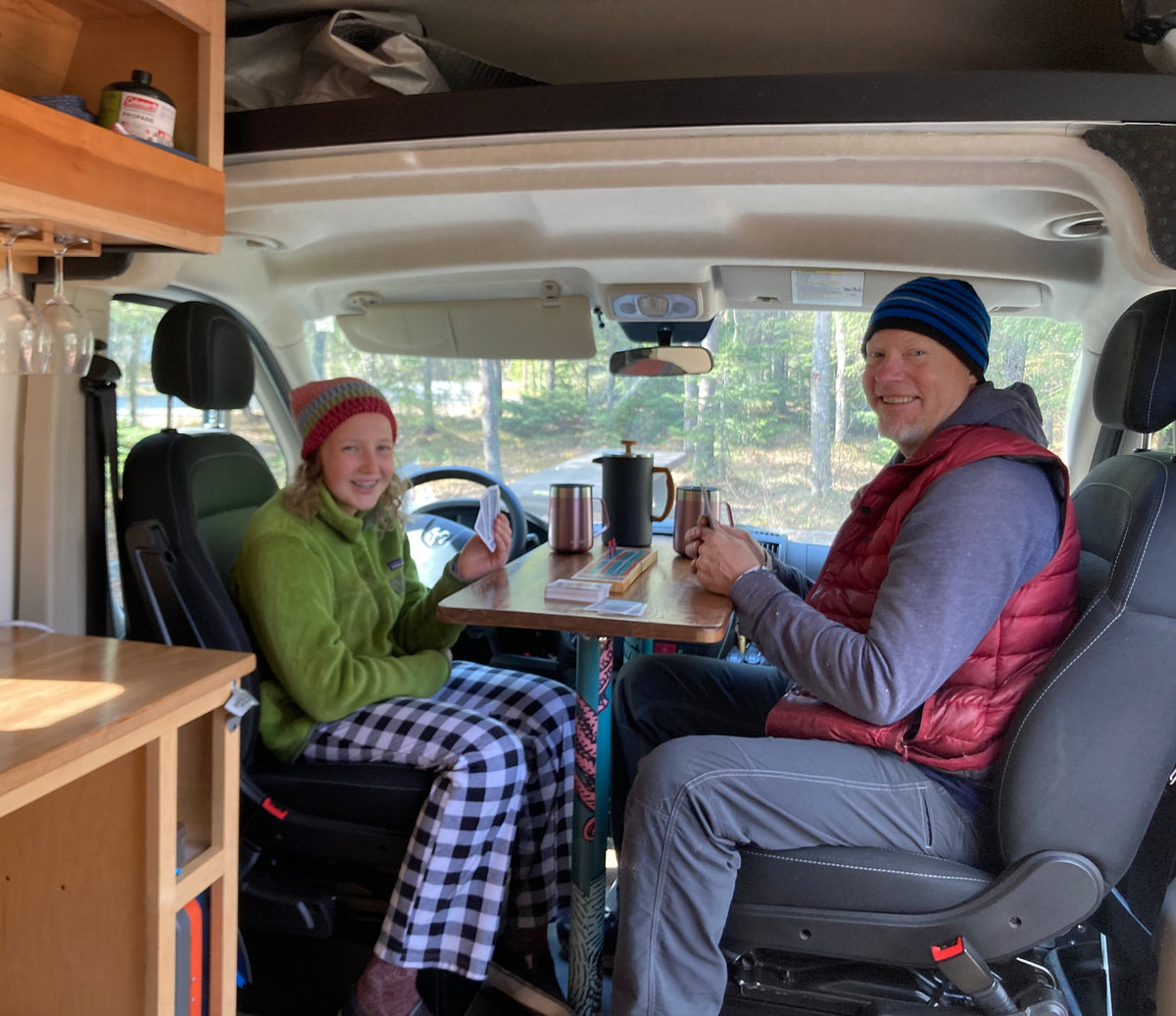 Smiling man and teen enjoy coffee and games in their RV rental. Cozy camper van interior for travel. — photo 9