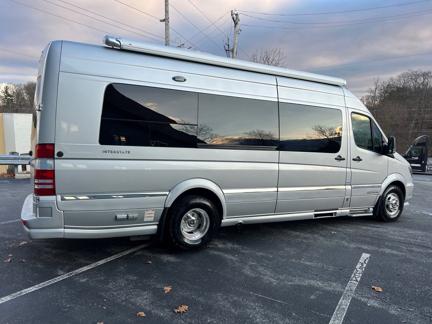 Sleek silver Airstream Interstate luxury RV rental, a spacious camper van, parked on asphalt with an awning extended.