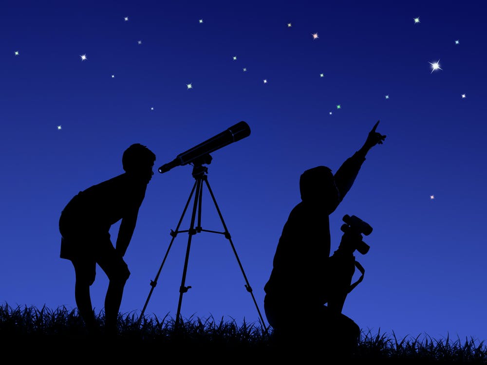 Experience astronomy! Two people with a telescope & binoculars observe a starry night sky. Perfect for your RV rental getaway.