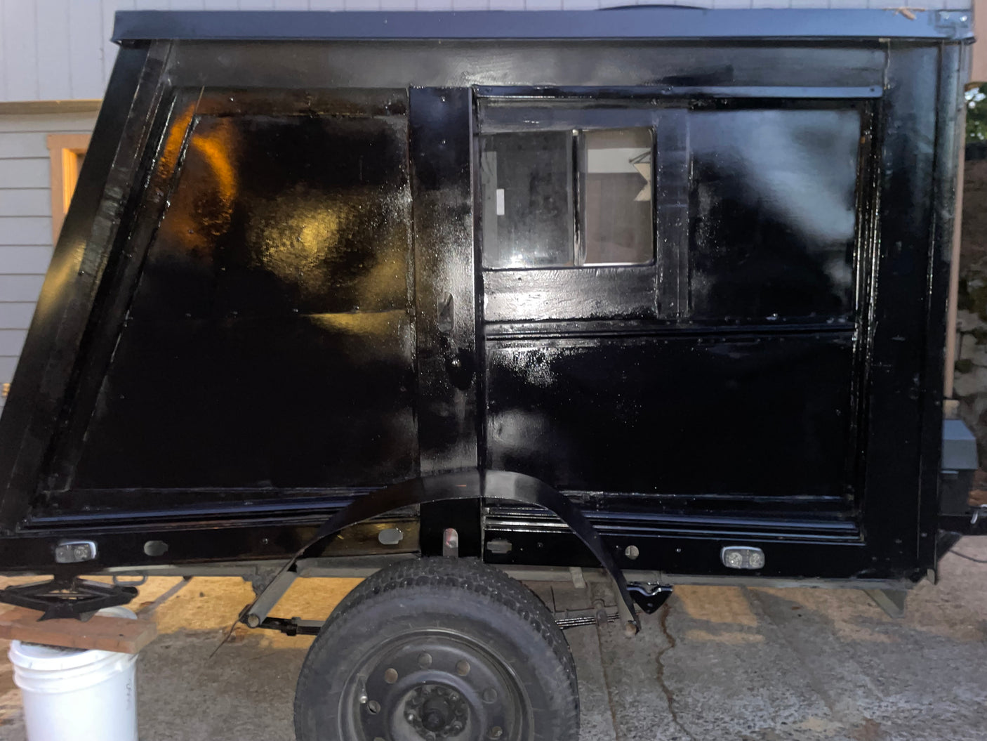 Custom-built black RV rental: a compact camper trailer with a window, wheel, and sturdy jack support.