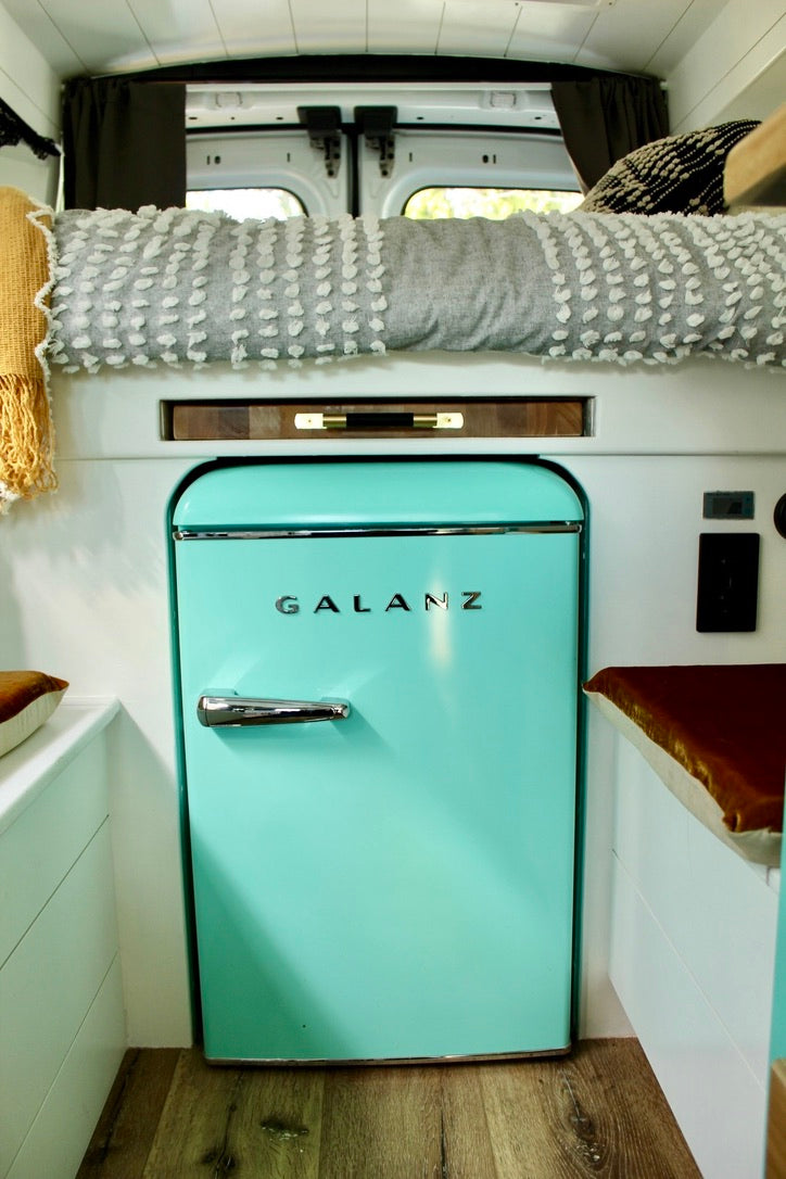 RV rental interior features a prominent retro aqua Galanz mini-fridge, cozy bed, and clever compact living space.
