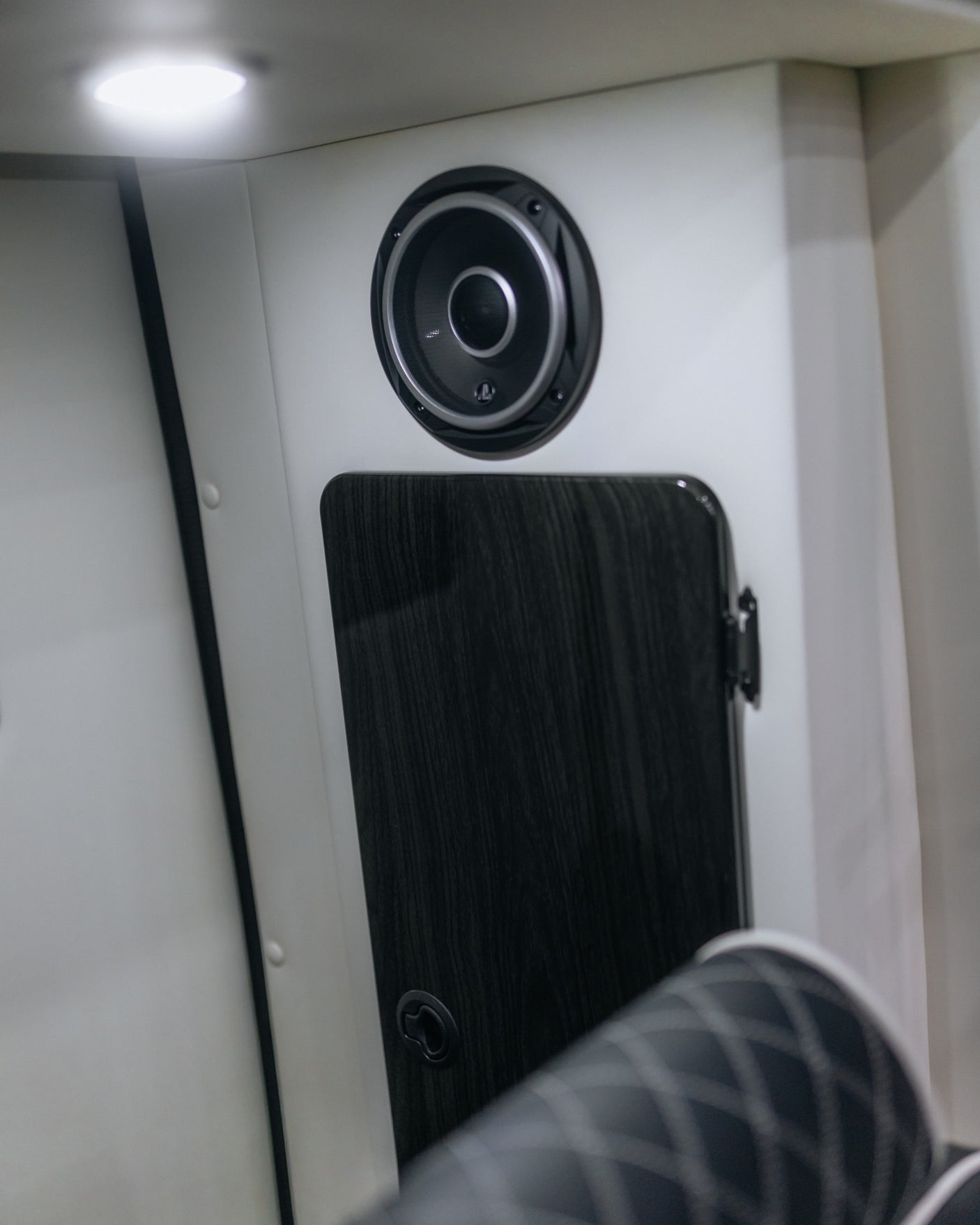 Modern **RV rental** interior featuring a wall-mounted audio speaker, dark wood-grain cabinet, and bright overhead light.