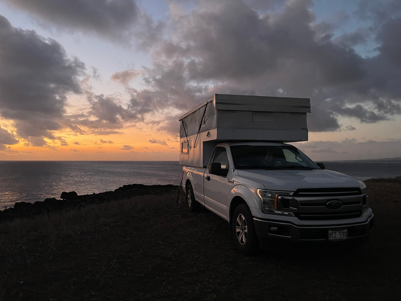 Coastal rv rental with a view: White truck camper parked by the ocean at sunset, showcasing a serene outdoor adventure.