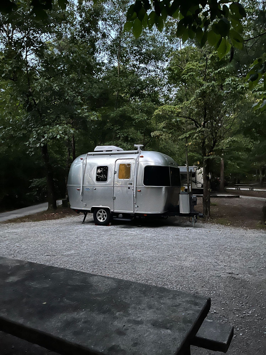 Cozy Airstream travel trailer RV rental parked at a serene forested campsite with warm interior lights glowing. Perfect outdoor getaway!|A shiny Airstream Bambi travel trailer