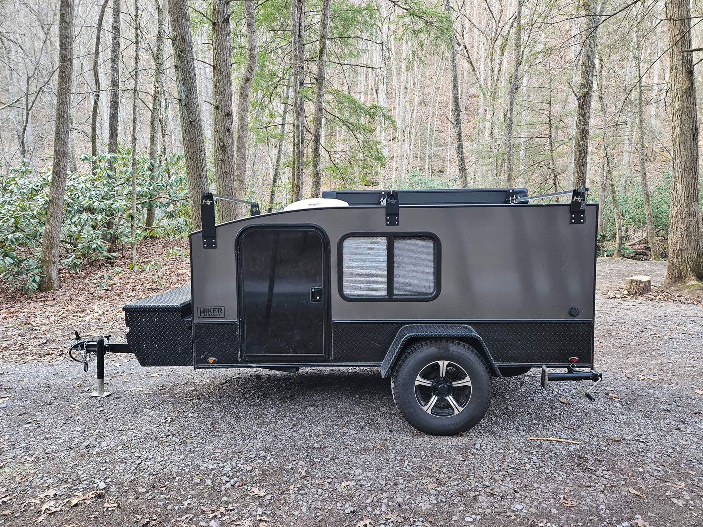 Dark gray Hiker teardrop camper parked at a wooded campsite, ready for your next RV rental adventure.
