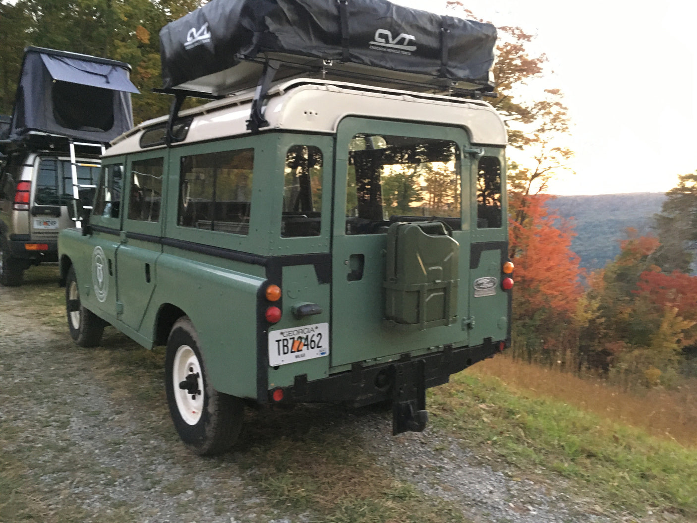 Classic green Land Rover with rooftop tent and jerry can, ready for rv rental adventures in autumn mountains.