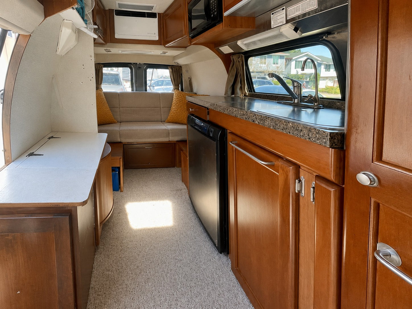 Interior of an RV rental: Features a kitchenette with sink, refrigerator, and a comfortable rear sofa/bed. Wood cabinetry.