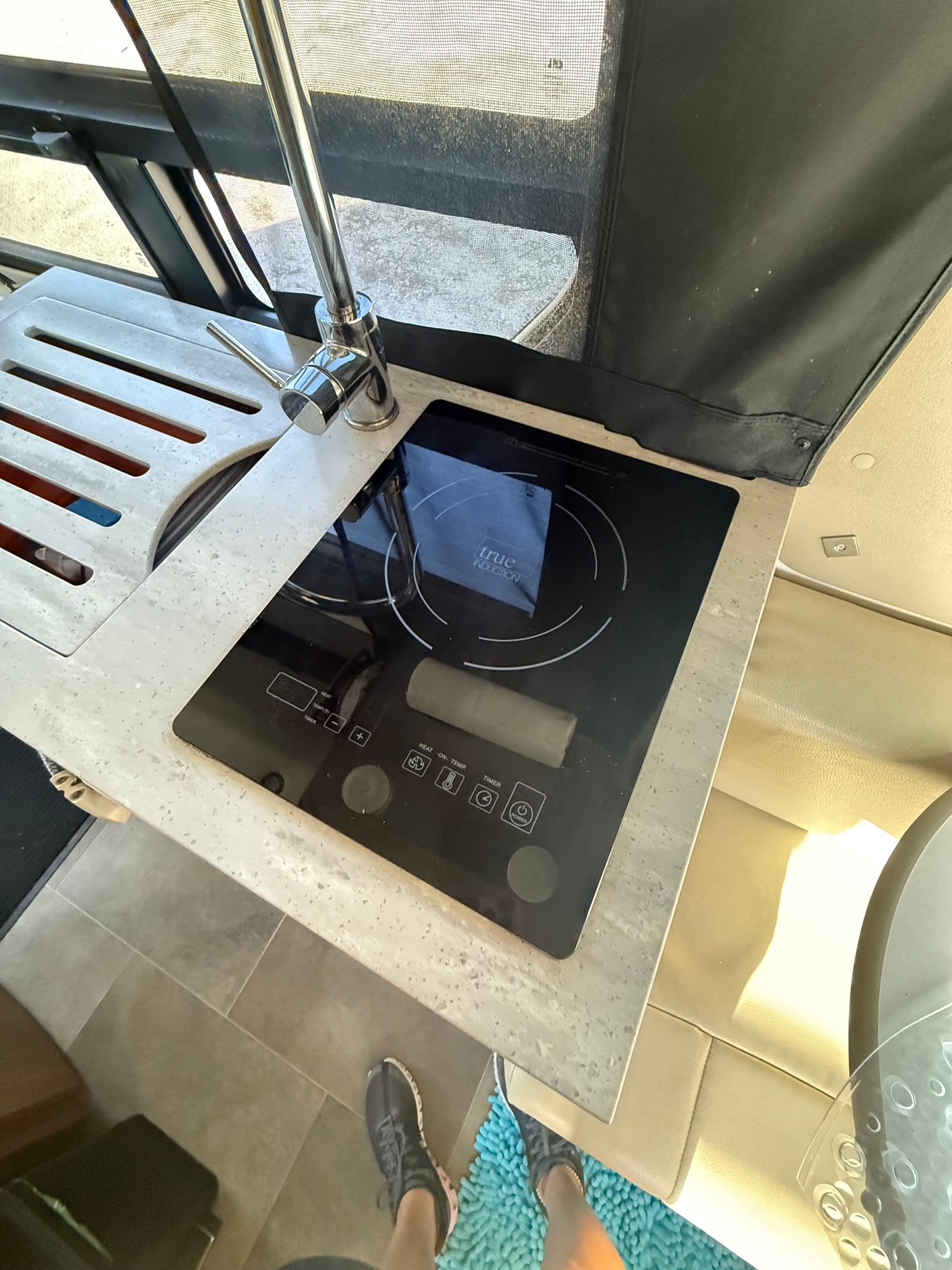Compact RV rental kitchen features a modern induction cooktop, sink, and stylish countertop, ideal for travel.