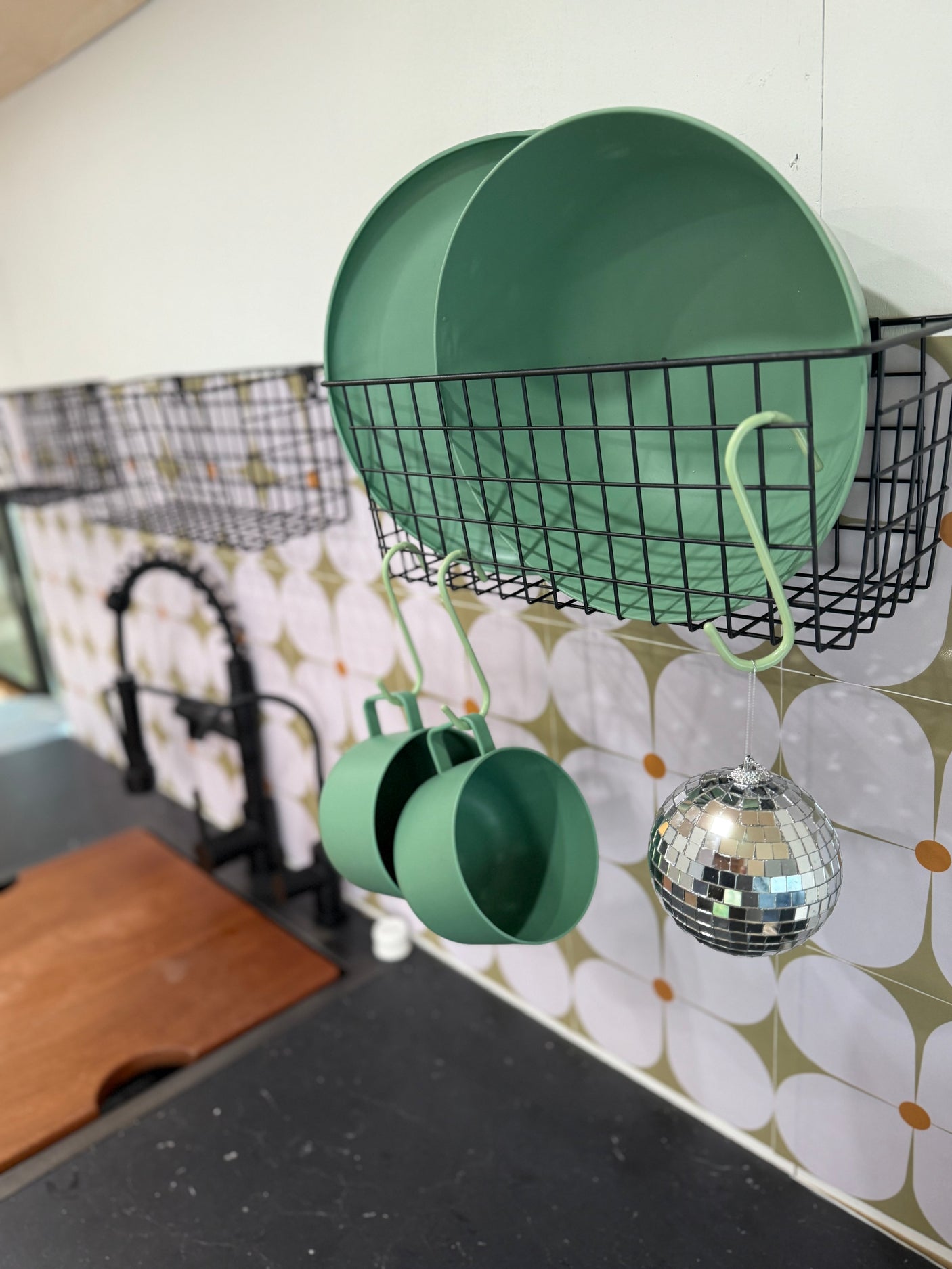 Compact RV rental kitchen storage: green plates, cups, & a fun disco ball hang on a patterned backsplash.