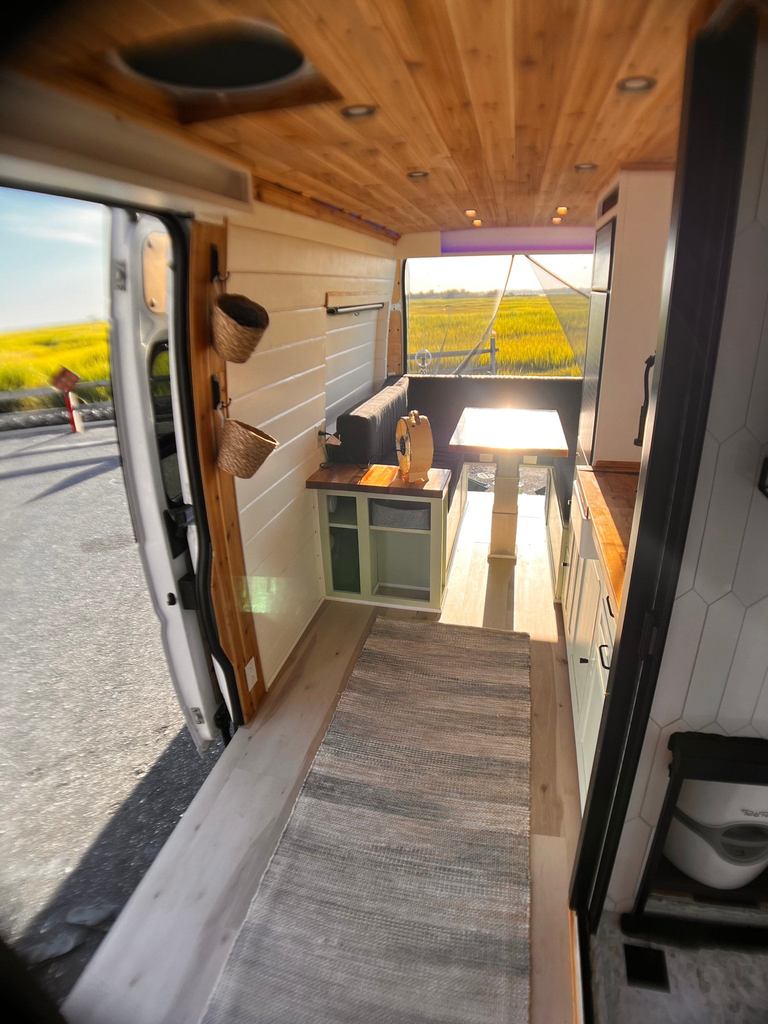 Step into this bright camper van RV rental. Featuring a wood-paneled ceiling, kitchenette, living space, and an open view to nature.