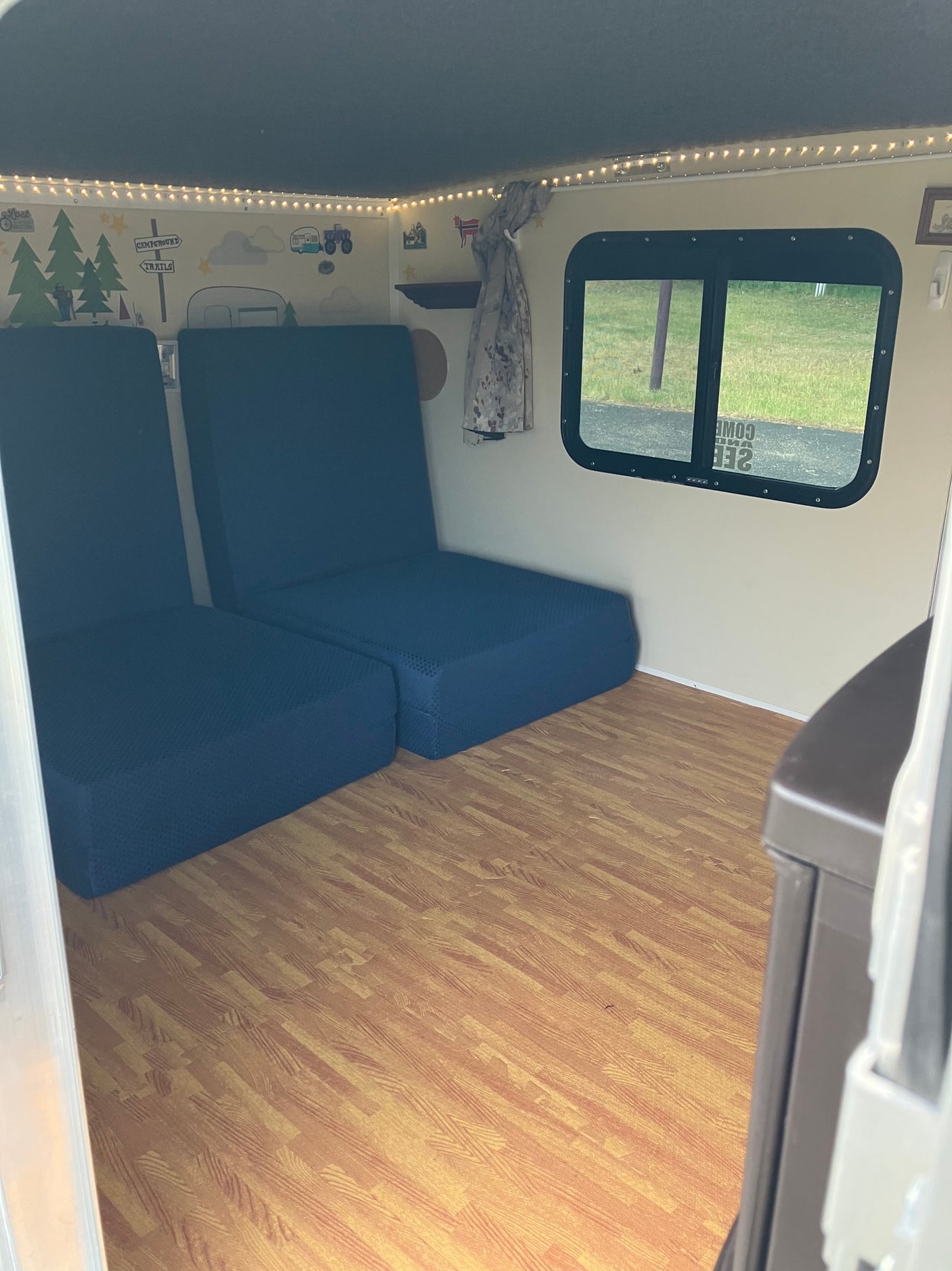 Versatile RV rental interior with convertible blue seating, wood flooring, and charming campsite wall decor.