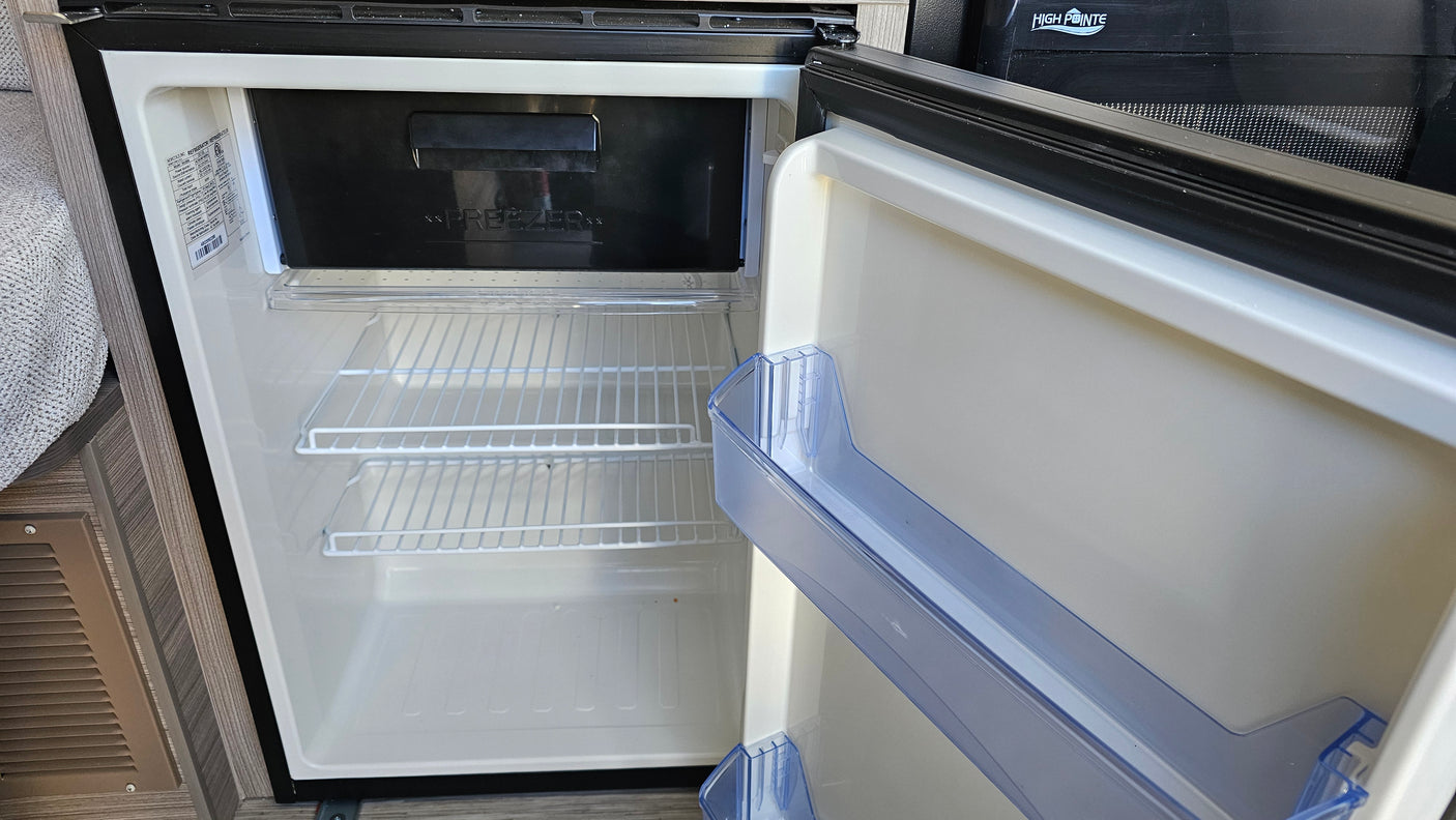 Open, empty compact refrigerator and freezer in an RV rental kitchen, ready for your trip.