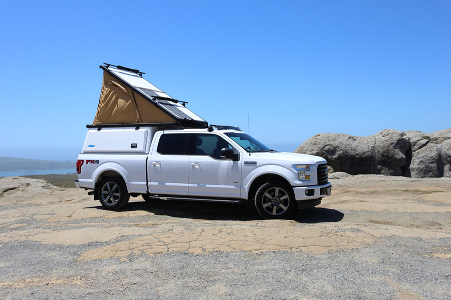 Adventure-ready RV rental: White Ford F-150 with pop-top camper, solar panels, and coastal views. Perfect for off-grid travel.