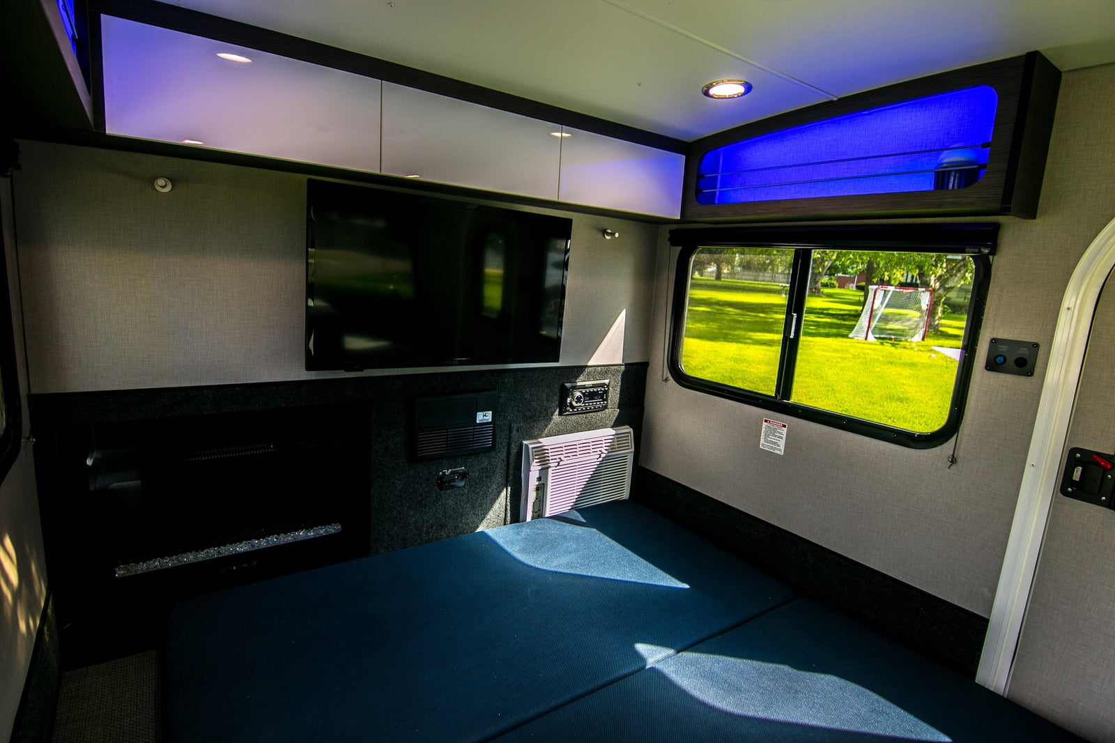 Modern rv rental interior with a cozy bed, TV, AC, and sleek storage. Bright lighting creates a welcoming space.