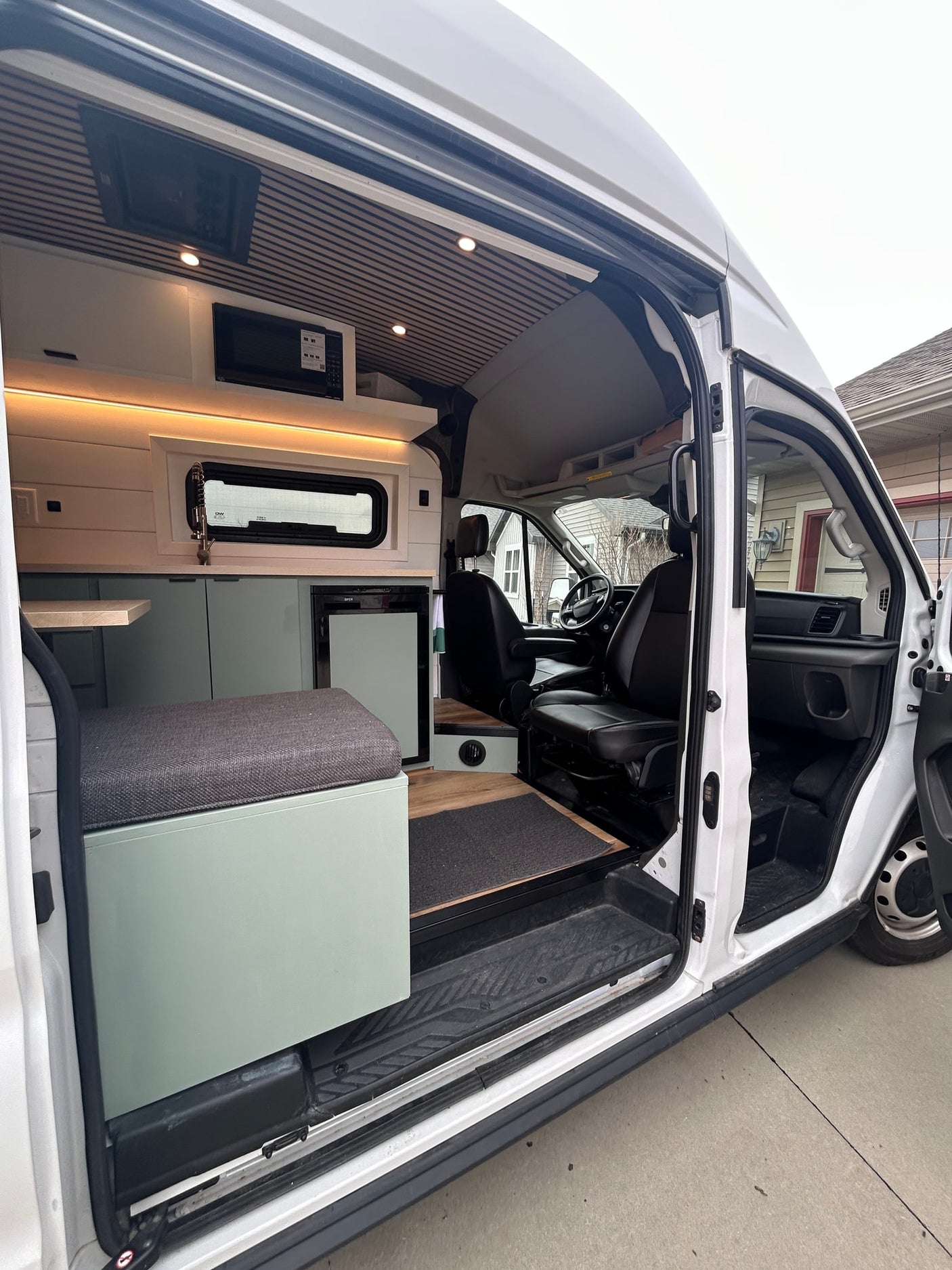 Inside an RV rental: a modern camper van with a kitchen, seating, and driver's area seen through the open side door.