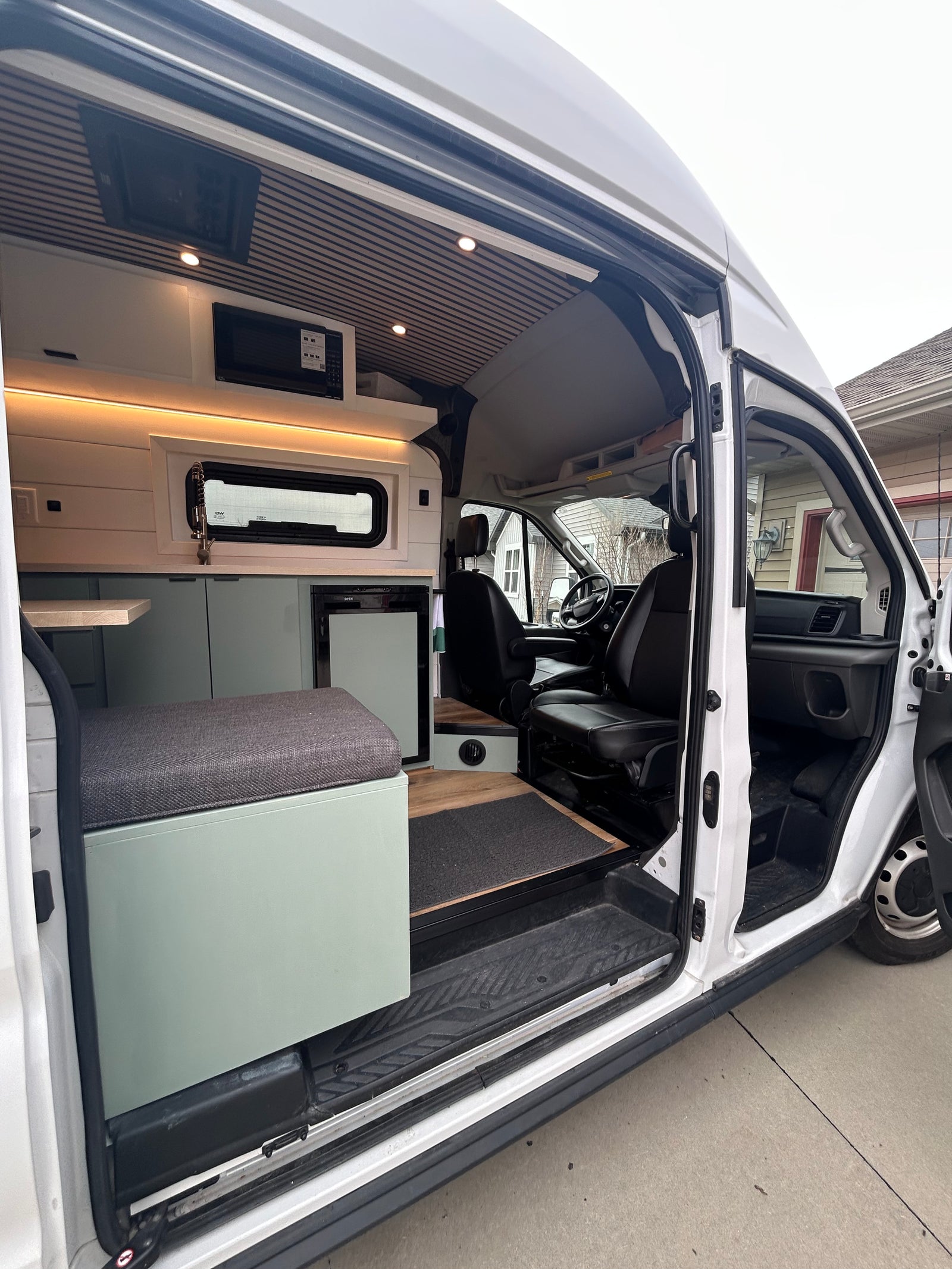 Inside an RV rental: a modern camper van with a kitchen, seating, and driver's area seen through the open side door.