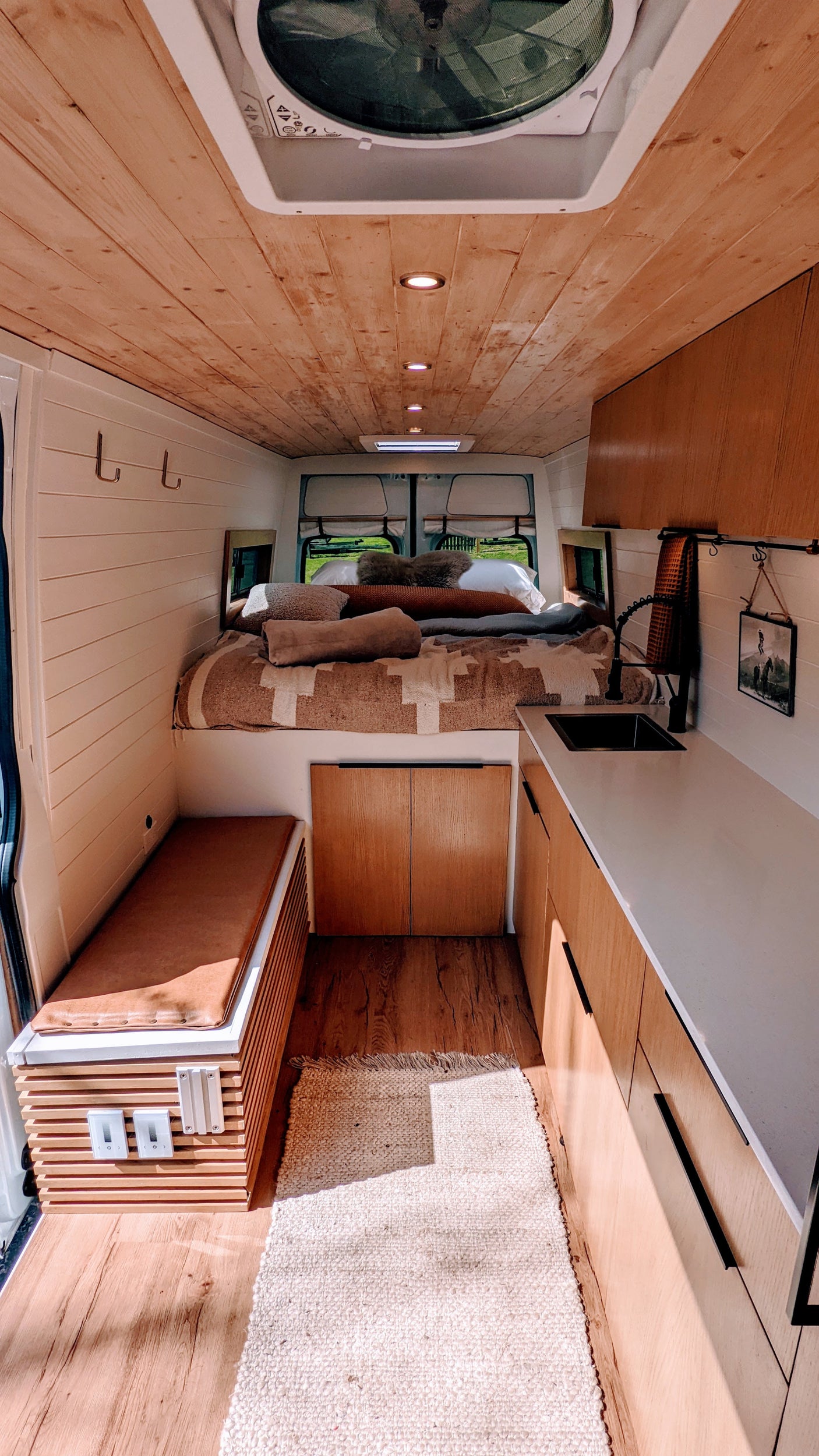 Cozy rv rental interior featuring a wood ceiling, shiplap walls, compact kitchen, and a comfy bed. Perfect for van life adventures!