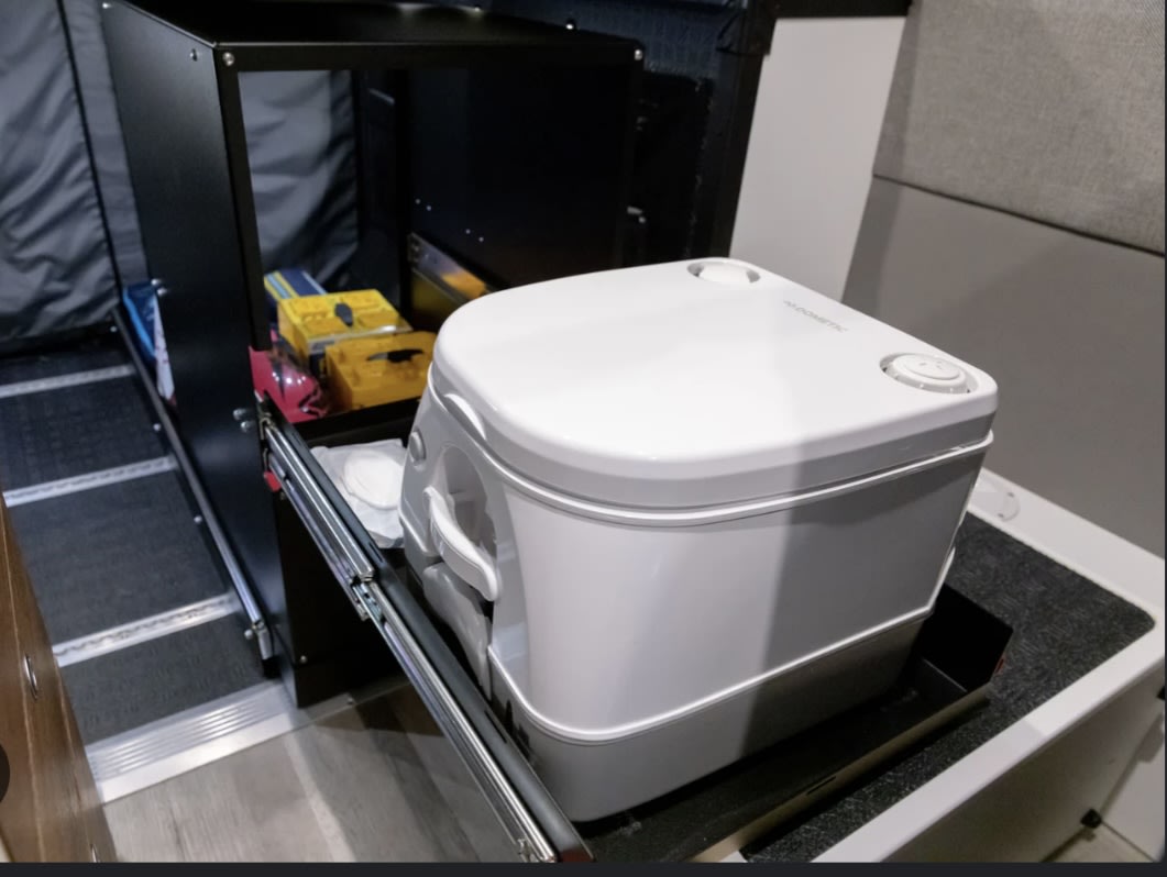 This rv rental features a compact Dometic portable toilet on a slide-out tray, revealing practical storage solutions.