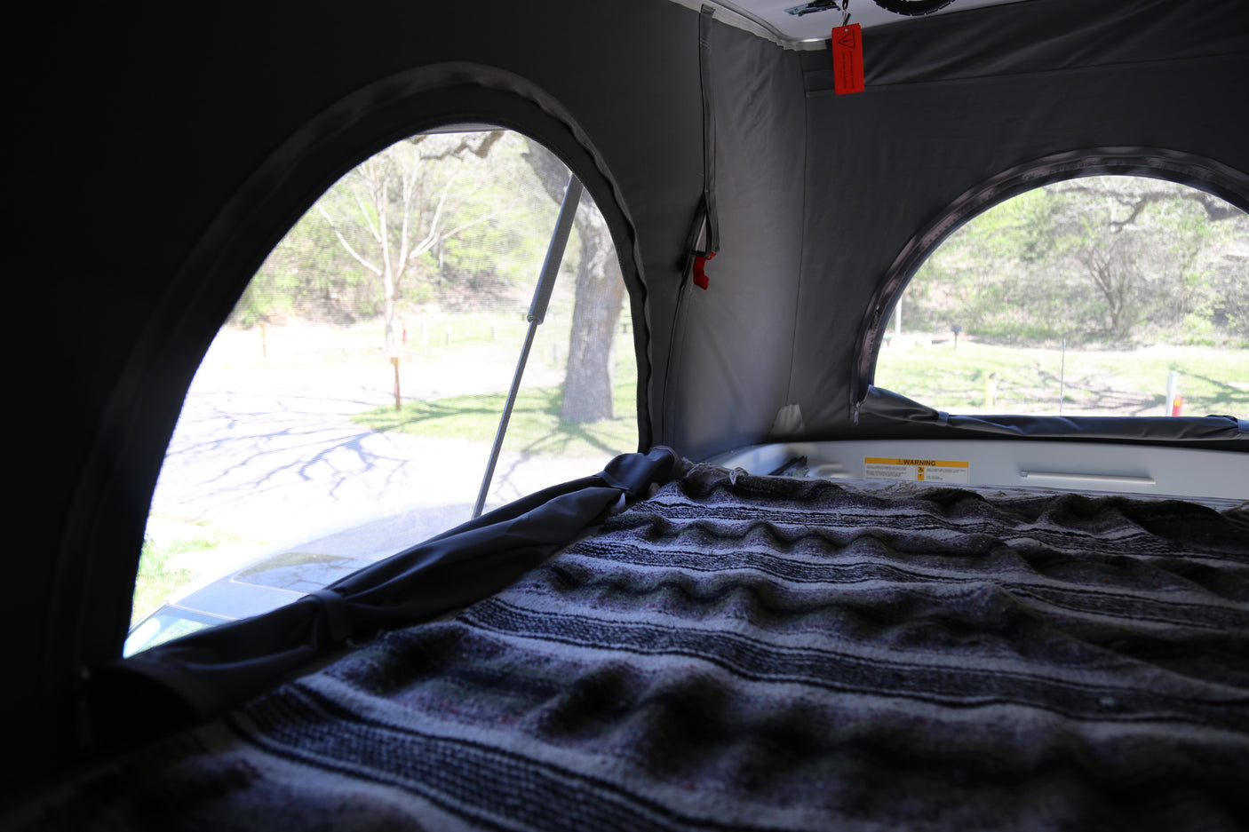 Pop-top RV rental interior: a comfy bed, screened windows, and a view of nature.