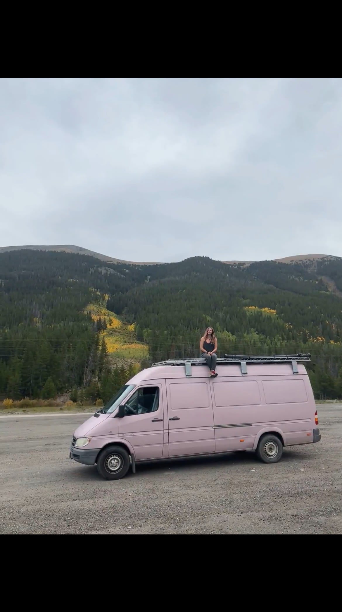 Woman enjoys mountain views from her pink RV rental camper van. Ideal for scenic road trip adventures in nature.
