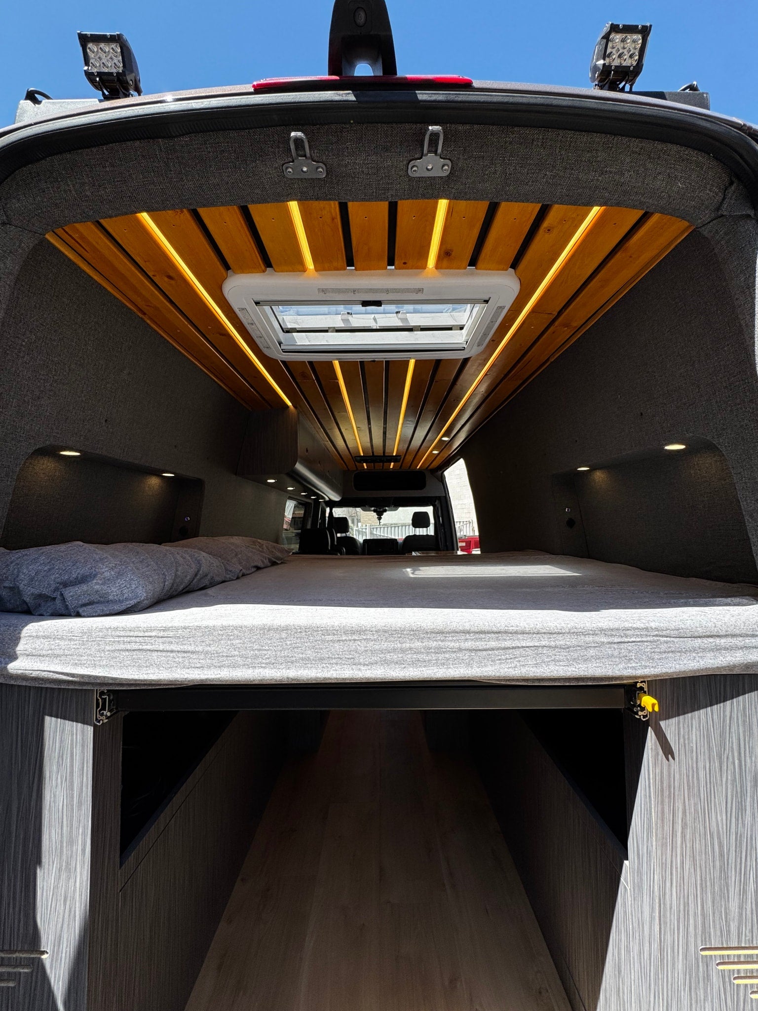Spacious custom RV rental interior features a cozy bed, ample storage, and stylish wood ceiling with lighting.