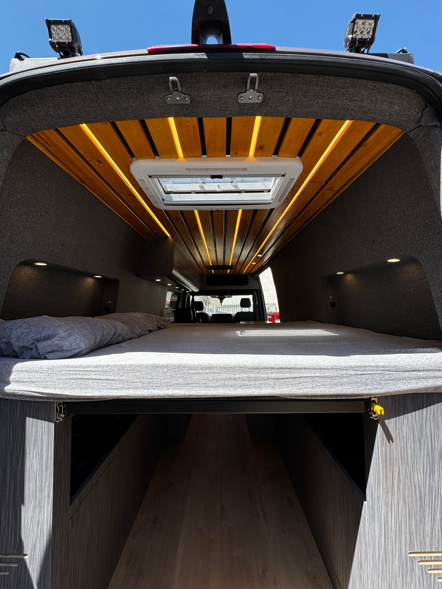 Spacious custom RV rental interior features a cozy bed, ample storage, and stylish wood ceiling with lighting.