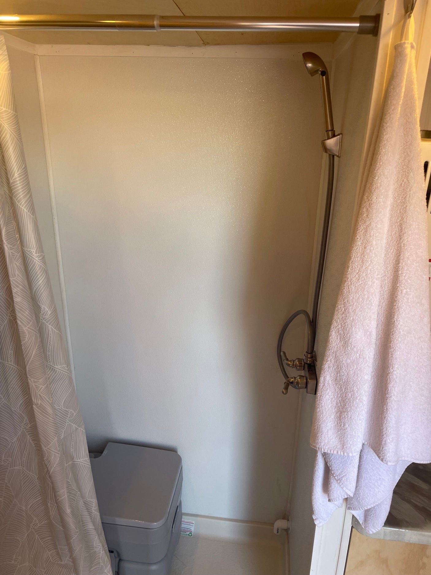 Inside an rv rental: a compact shower with a wall-mounted head, portable toilet, and shower curtain.