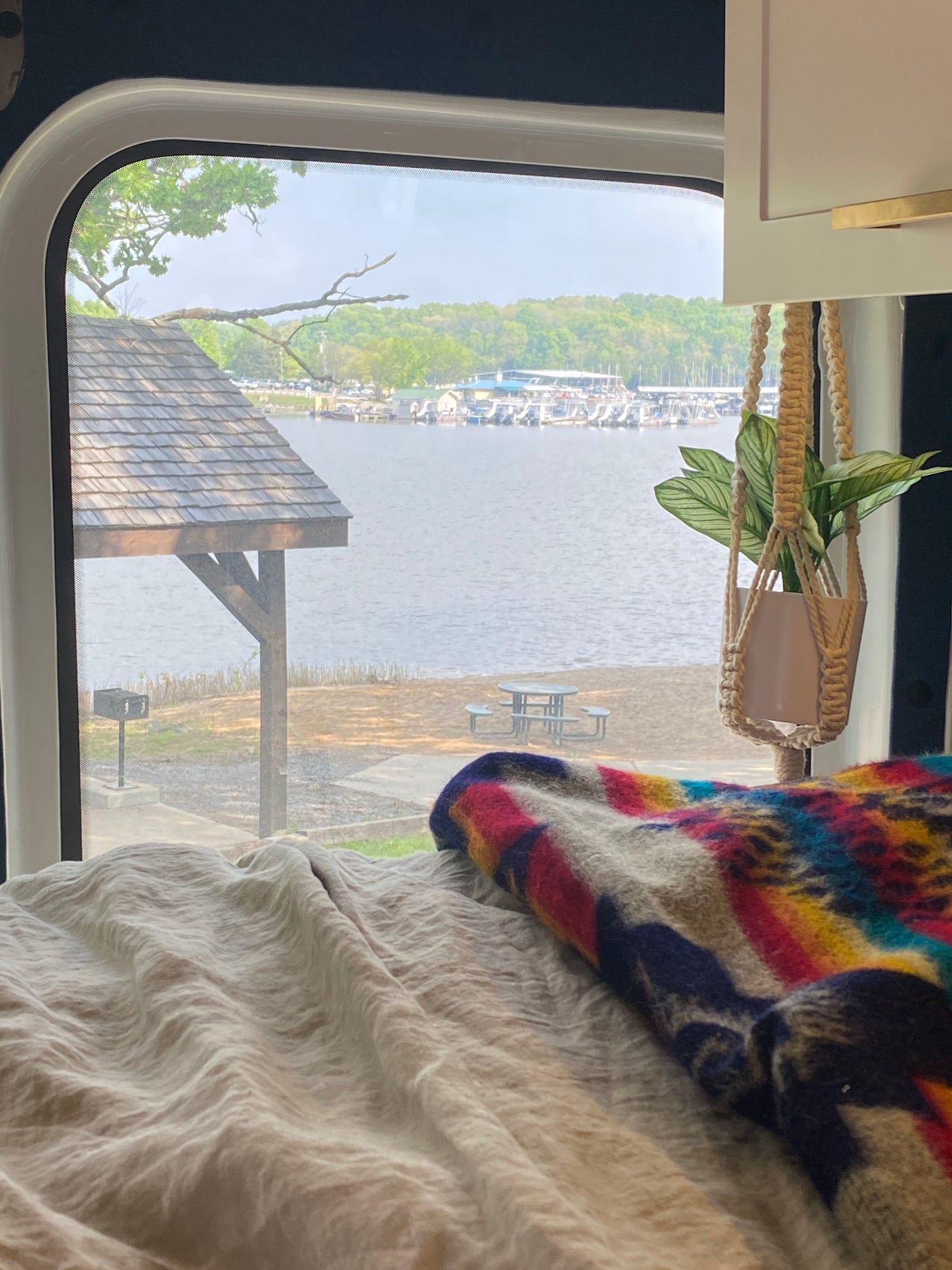 Enjoy a serene lake view with boats and beach from a cozy RV rental bed. Perfect nature escape!