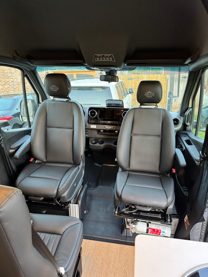 Storyteller Overland rv rental interior: Front seats, dashboard, and overhead controls visible, with a fire extinguisher.