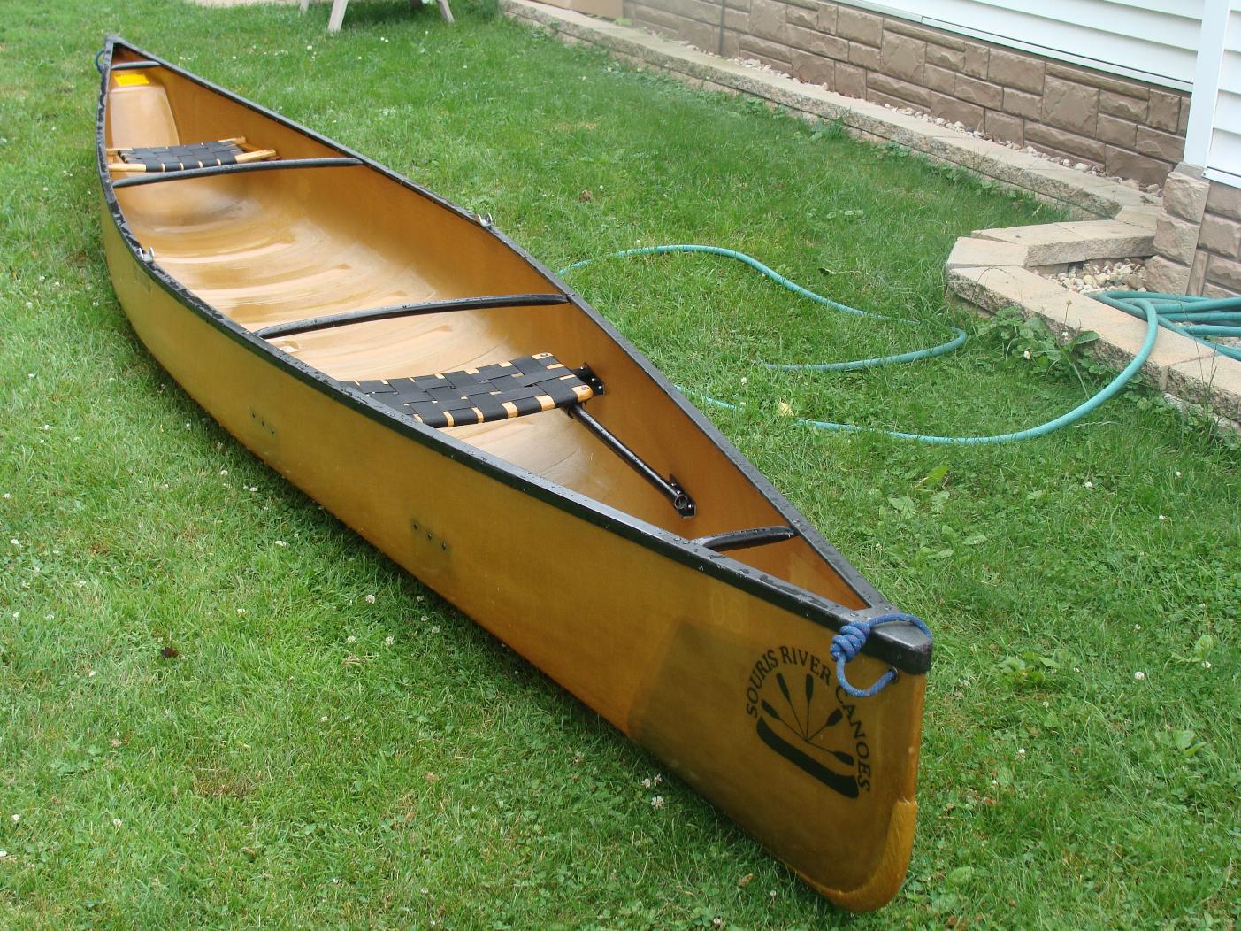 Yellow canoe with black trim and "Souris River Canoes" logo on green grass. Ideal for an RV rental outdoor trip.