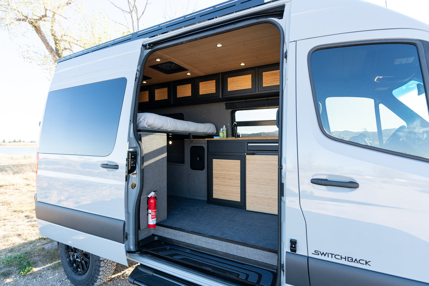 Explore this modern RV rental's inviting interior: an open camper van with a comfy bed, kitchen, and wood-paneled storage.