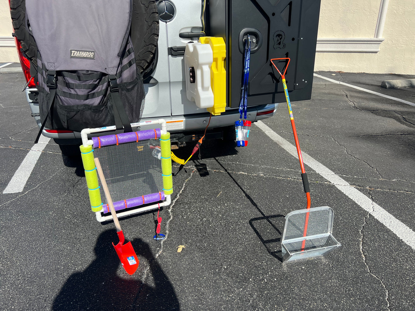 RV rental equipped with outdoor gear: TRASHAROO bag, jerry cans, and various sifting tools for beach adventures.