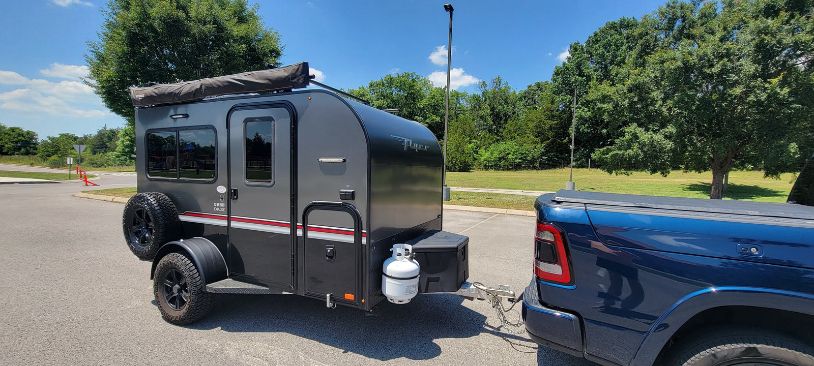 Dark grey teardrop rv rental trailer hitched to a blue pickup, ready for adventures on a sunny day.