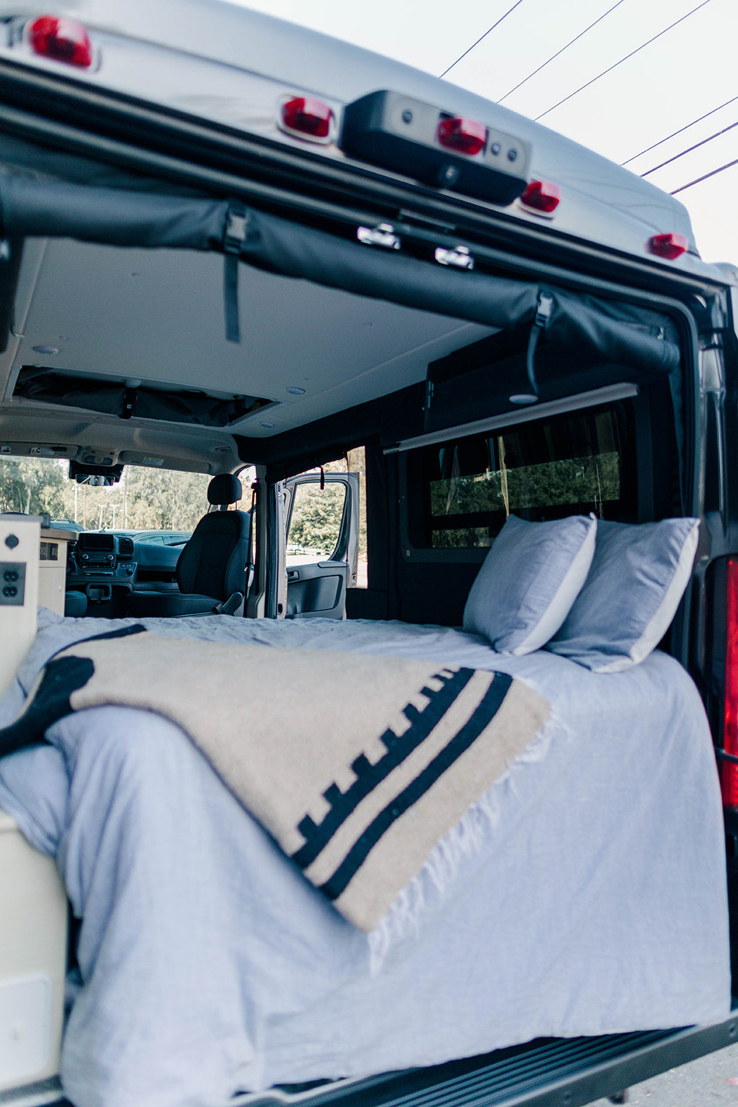 Cozy camper van bed inside an RV rental, ready for adventure. View the comfortable interior looking towards the dashboard.