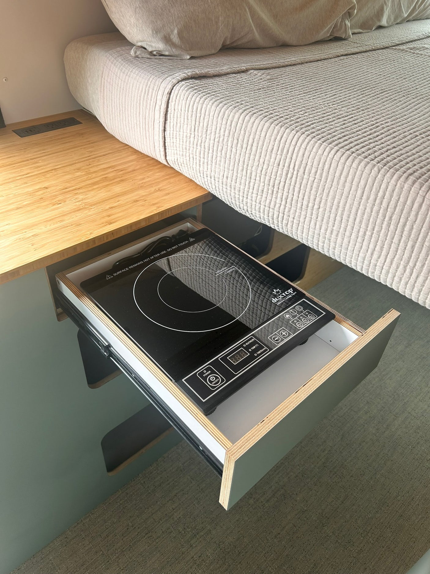 Compact RV rental setup: bed, countertop with power, and a pull-out induction cooktop for efficient cooking.