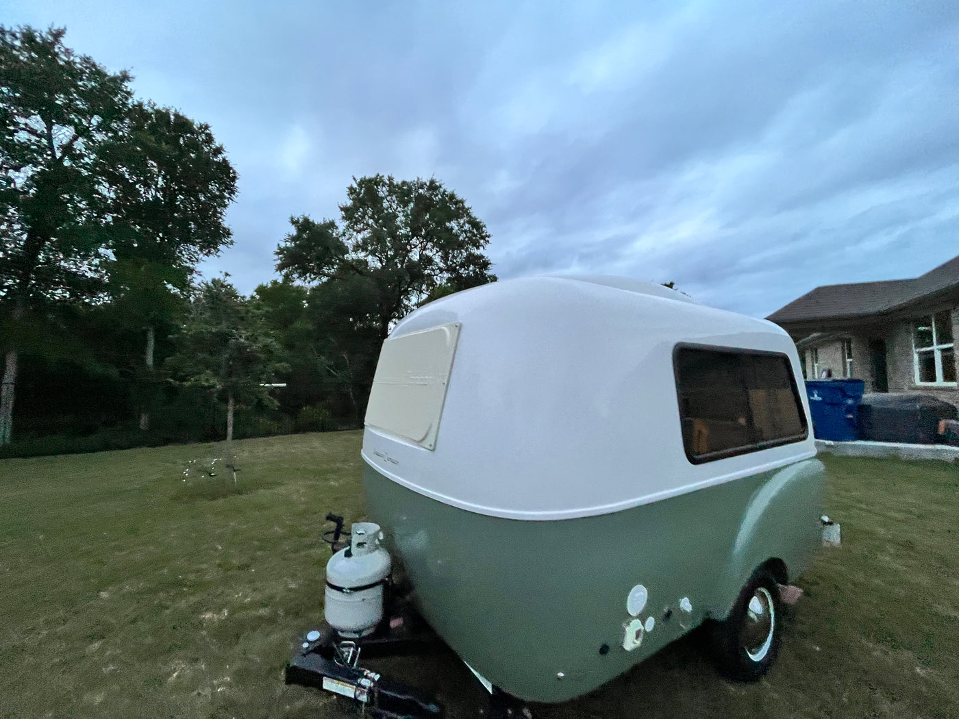 This charming white and sage green teardrop RV rental is ready for adventure, parked in a grassy yard under an overcast sky. — photo 6