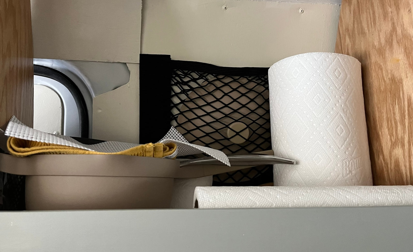 RV rental: Compact storage with paper towels, a mesh net, and stacked dishes with cleaning supplies.