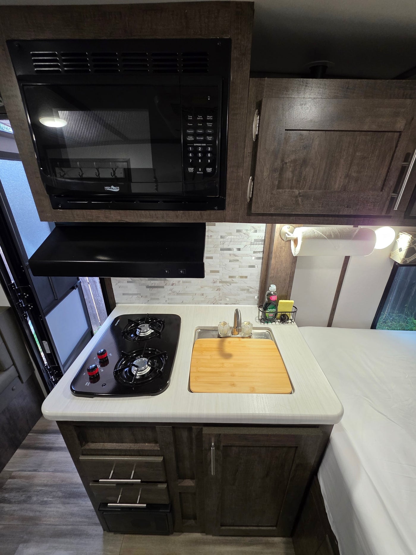 Modern RV rental kitchenette: High Pointe microwave, 2-burner stove, sink, and storage. Ideal for travel. — photo 7