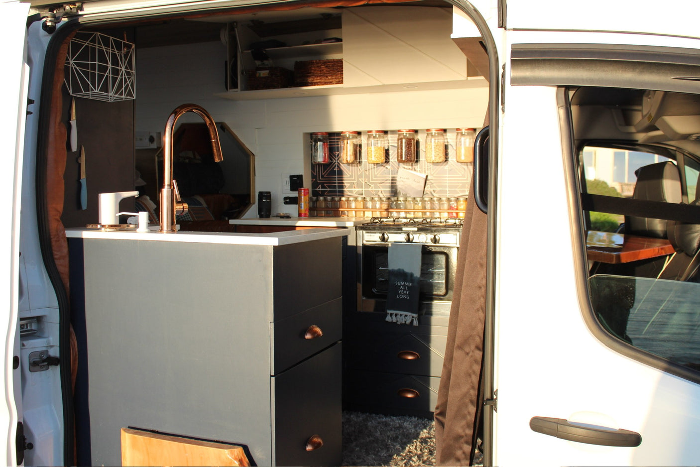 Inside this RV rental: modern van kitchen with copper faucet, stove, organized spices, and clever storage.