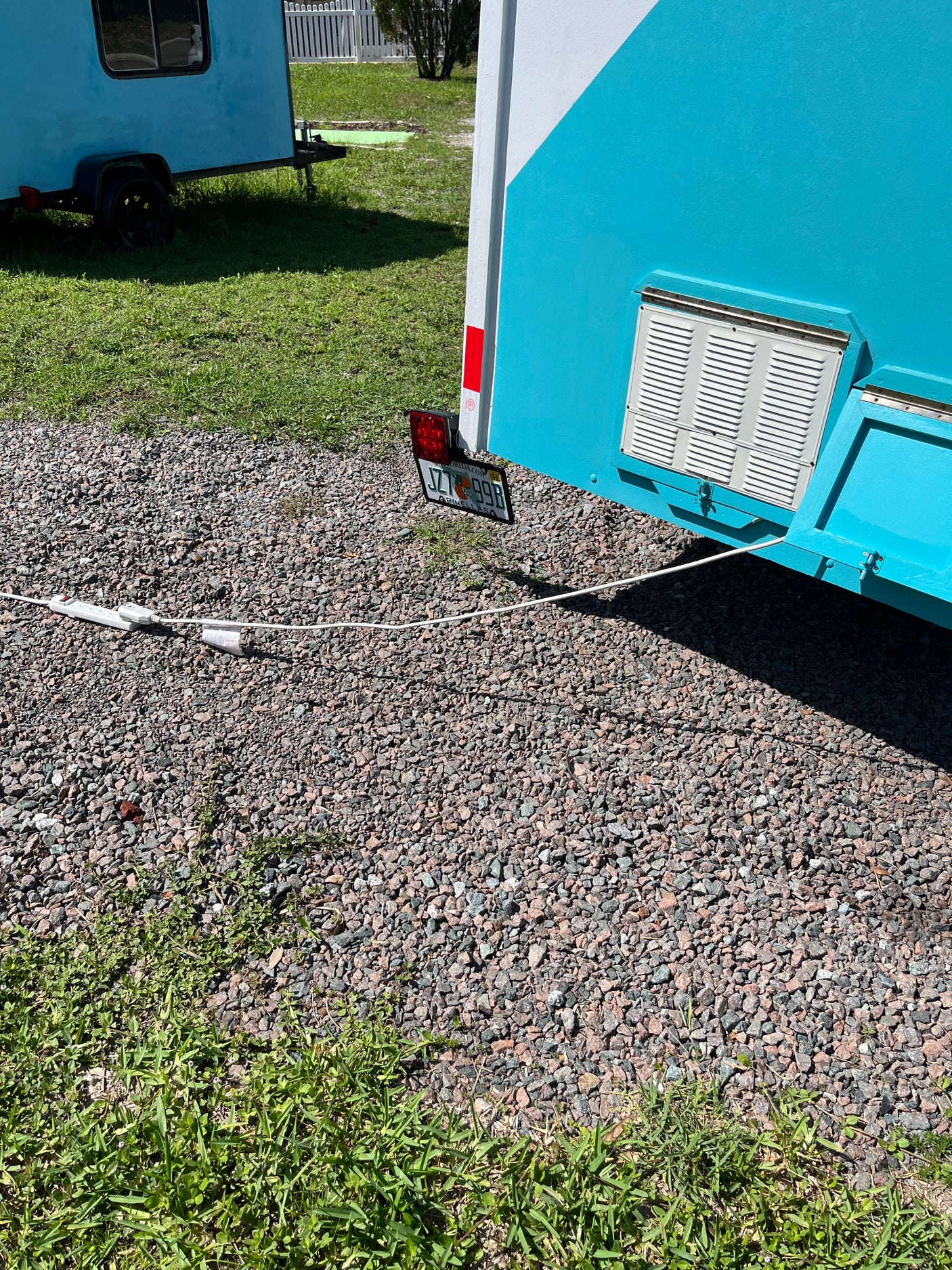 Two compact blue trailers for an RV rental. One has a Florida plate & vent; both sit on a gravel and grass lot with a power cord.