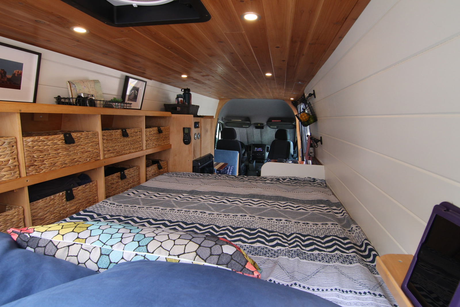 Inside a stylish RV rental, showing the bed, wood ceiling, white walls, and built-in storage with wicker baskets.