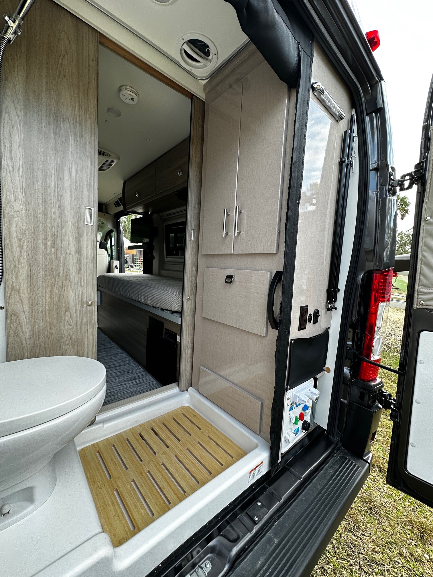 Inside this modern RV rental: open rear view reveals compact kitchen/storage, control panel, and bathroom beyond.